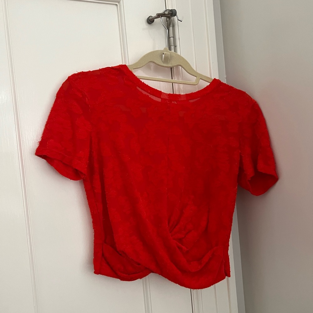Short sleeve sheer red top with draping detail on the bottom to expose mid drift
